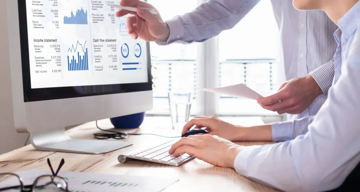 Two professionals reviewing a balance sheet, income statement and cash flow statement together on screen