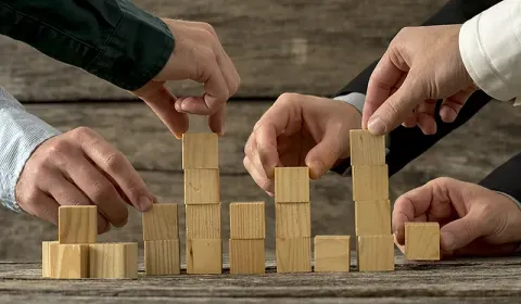 Business partners stacking wooden blocks together, symbolizing steady step-by-step growth