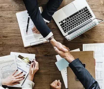 Business partners shaking hands over a laptop while agreeing on a company structure
